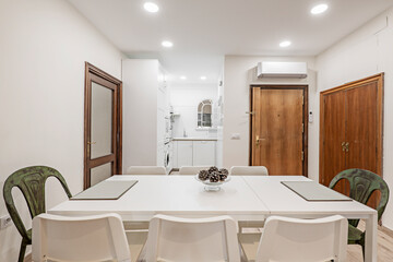 Dining room with eight chairs and open kitchen in the background and cupboard built into one wall