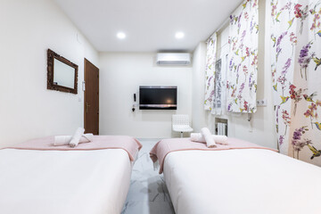 bedroom with two separate beds, tv on one wall, air conditioner and curtains seen on the windows