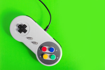 Close up photo of classic wired gray colored 8 bit game pad controller laying on green background. © breakermaximus