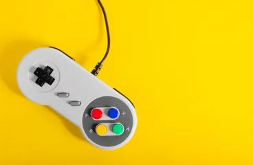 Foto auf Leinwand Photo of classic gray colored 8 bit game pad controller laying on yellow background. © breakermaximus