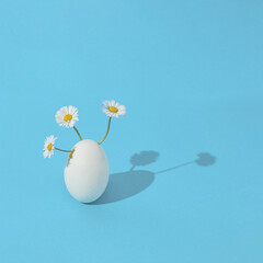Flowers with egg on a blue background. Easter aesthetic creative idea. Surreal composition