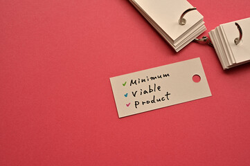 There is a small card placed on a red background paper with the word Minimum Viable Product written...
