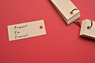 There is a small card placed on a red background paper with the word Request for Proposal written...