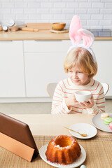 Vertical portrait of cute boy wearing bunny ears while enjoying breakfast on Easter morning and...