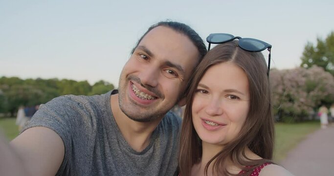 A young beautiful couple of tourists with braces make selfies in the park.