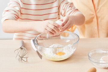 Close up of child breaking eggs while helping mother baking in kitchen, copy space