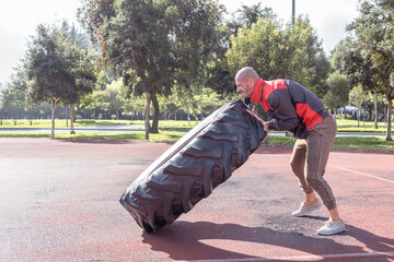 Bald man lifting and pushing a huge wheel exercising outdoors