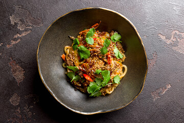 fried Udon with beef and vegetables on black bowl on dark stone table top view