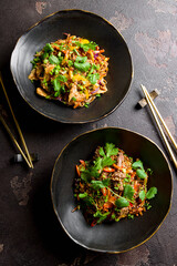 chicken wok noodles with vegetables and sesame and wok with fried beef and vegetables on black bowls on dark stone table top view