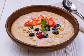 amaranth porridge with fresh berries,nuts and mint on brown bowl on white wooden table macro close up