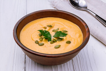 Soup cream of pumpkin with pumpkin seeds macro close up on white wooden table