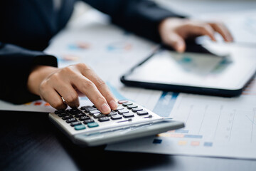 Close up of Businesswomen or Accountant using a calculator and laptop computer with analytic business report graph and finance chart at the workplace, financial and investment concept.