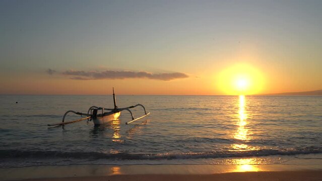 Time lapse of unknown fishing boat on a tropical beach with golden sea background at beautiful sunrise with calm feeling in Indonesia. 