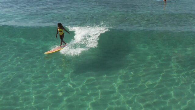 Charming curly African-American dark-skinned young woman, a professional surfer rides a wave on a long surfboard in the ocean, aerial shot from above