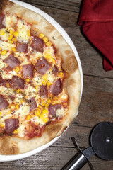 Pizza lista para comer con salsa roja, queso mozzarella, maíz, tocineta y orégano en un plato blanco sobre un fondo de madera