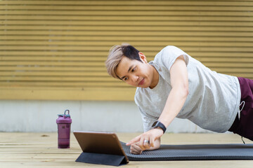 Fototapeta na wymiar Happy Asian young man doing a plank exercise and watching on a tablet.