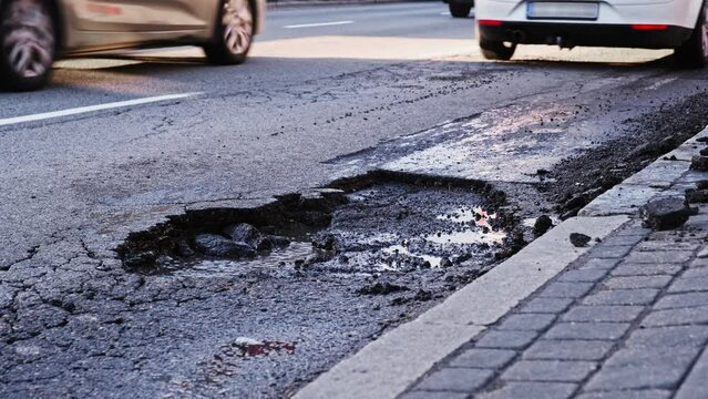 Vehicles Driving Over Deep Large Erosion Hole in City Street Asphalt after Severe Weather and Heavy Rainfall Risking of Damage to Car Tyre and Suspension
