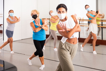 Naklejka na ściany i meble Dancing asian woman in a protective mask, engaged in group training during a pandemic, practices energetic swing in a modern ..dance studio