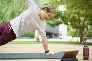 Happy Asian young man doing a plank exercise and watching on a tablet.