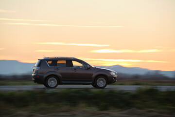 Fototapeta na wymiar SUV car driving fast on intercity road at sunset. Highway traffic in evening