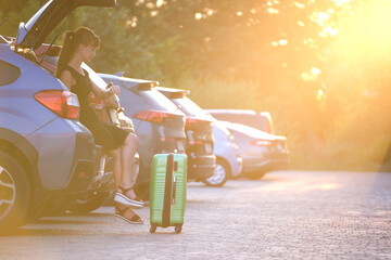 Young woman with suitcase bag waiting beside car. Travelling and vacations concept