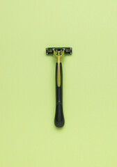 The minimal composition is a black and green men's razor on a green background. The central composition. Flat lay.