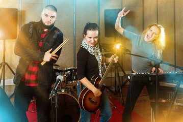 Fototapeta na wymiar Three cheerful smiling bandmates posing together with musical instruments in rehearsal room