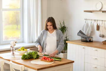 Obraz na płótnie Canvas a young pregnant woman makes herself a salad of fresh vegetables, the concept of proper nutrition