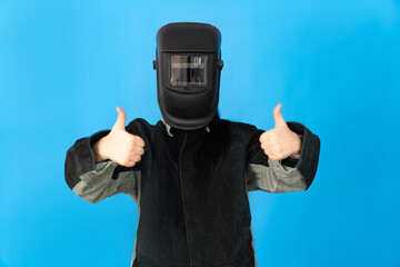 a welder girl in a protective mask looks into the camera and shows a thumbs up.