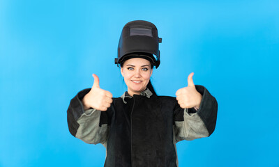 a welder girl in a protective mask looks into the camera and shows a thumbs up.
