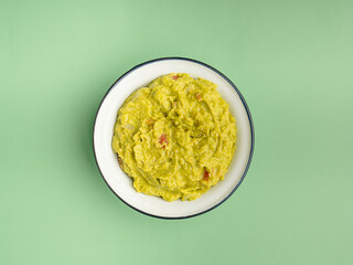 Fresh guacamole in a bowl over a green background