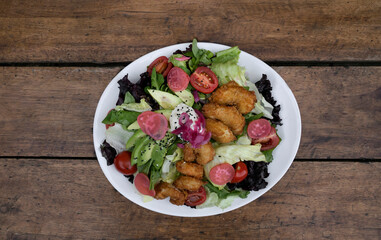 Gourmet salad. Top view of a fresh sea salad with lettuce, cherry tomatoes, avocado, radish and onion pickles, seeds and cream cheese, in a white dish on the wooden table.
