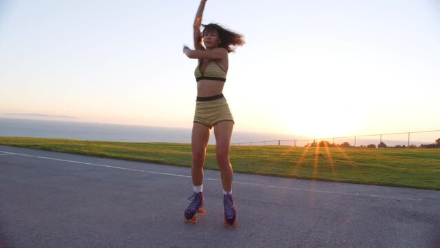 Astonishing, modern dance on roller skates by professional female dancer. Pretty young woman enjoys summer outdoor workout with the ocean in the background. High quality 4k footage