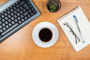 Coffee at work or office, a cup of coffee on the desktop, computer keyboard and office supplies, top view, space for text