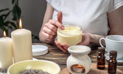 Woman is smearing her hands with a natural organic cream doing a massage. Aroma lamp with essential oils and candles on the table. Concept of skin and self care in atmosphere of harmony and relaxation