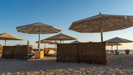 Sunny morning on the beach of the Red Sea. Lattice umbrellas against blue sky. Empty sun loungers on the sand. Light and shadow. Egypt. Safaga
