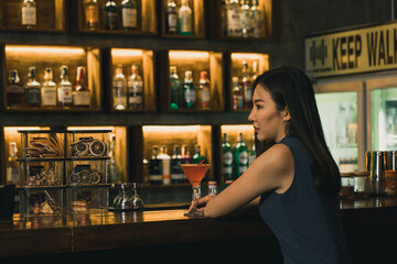 Asian woman drinking a cocktail at a bar at night.