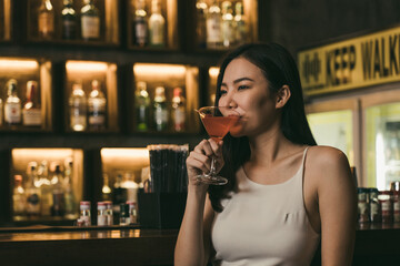 Asian woman drinking a cocktail at a bar at night.
