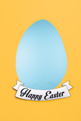 Vertical image of Easter greeting card with shape of light blue egg and regards of happy holiday below and yellow copyspace around