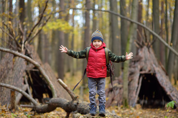 Little boy scout during hiking in autumn forest. Behind the child is teepee hut. Adventure,...