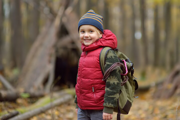 Little boy scout during hiking in autumn forest. Behind the child is teepee hut. Adventure,...
