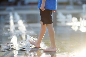 Close-up of little boy legs between the water jets in the dry fountain at sunny summer day. Active...