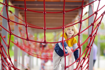 Cute preschooler boy having fun on outdoor playground. Spring summer autumn active sport leisure...