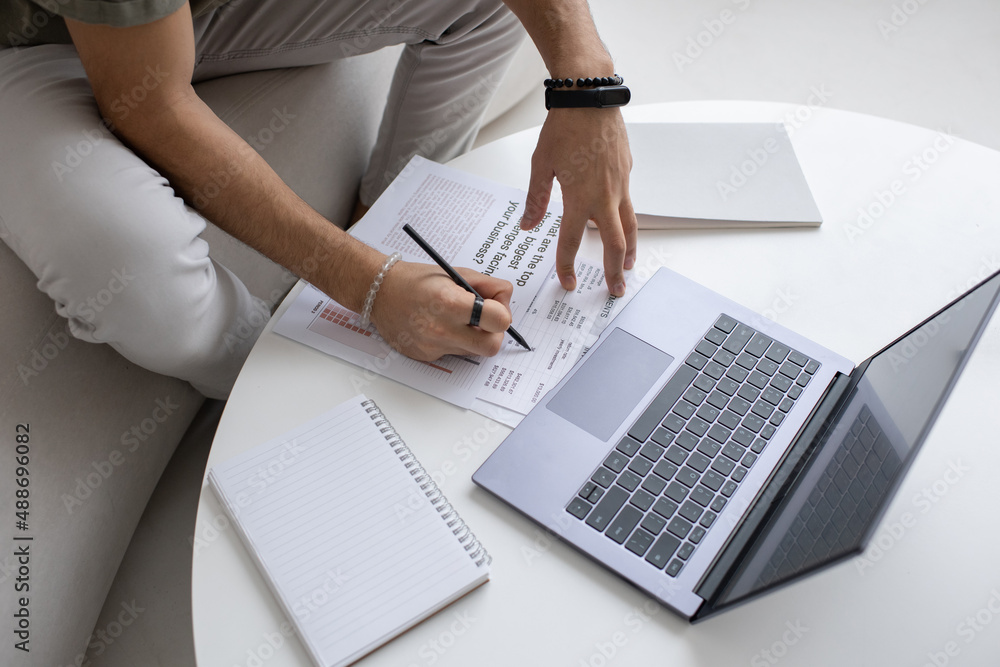 Poster hands of young economist or analyst with pen pointing at financial document while analyzing data in 