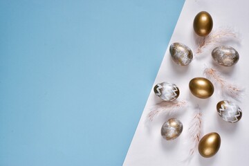 Banner. Golden eggs and feathers on a blue and white background. Minimal concept. Card with copy space for text. Flat lay composition. Happy easter