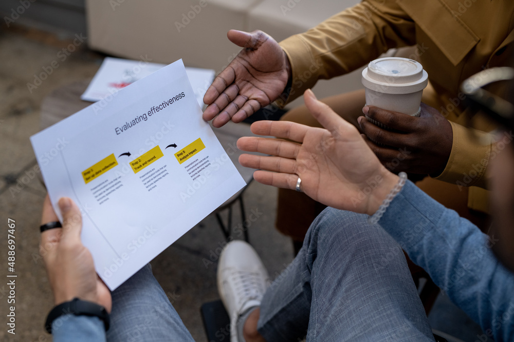 Poster hands of two contemporary intercultural businessmen discussing paper with evaluation data and pointi