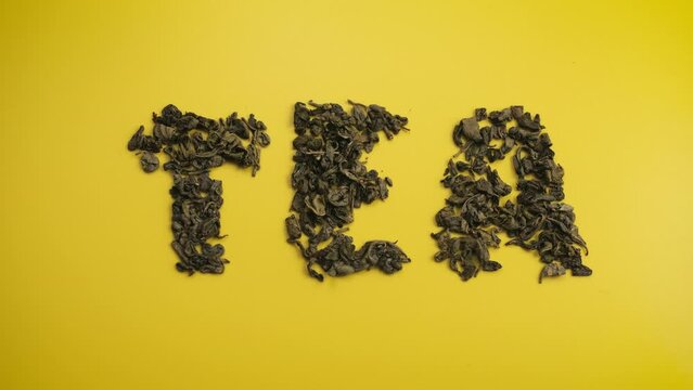 Word tea by the moving dry leaves of the brew falling from above. Shot from above against a yellow background. Flatlay stop motion animation