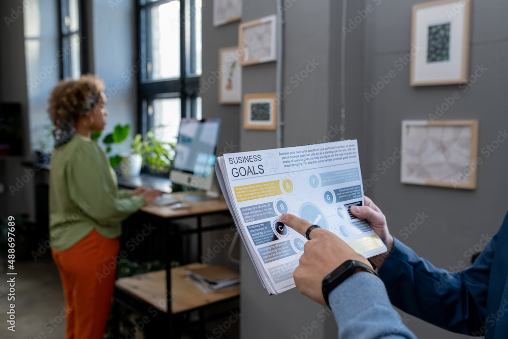 Poster hand of young businessman pointing at paper with business goals while discussing it with colleague d