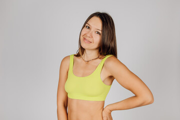 Portrait of beautiful Caucasian woman. Beautiful elegant tanned brunette in yellow underwear, smiling at camera, posing on isolated gray background, concept of body acceptance and beauty.