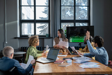 Young Asian businesswoman with papers talking to one of colleagues during discussion of presentation or project points at meeting